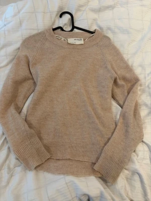 Beige stickad tröja från Selected Femme - Mysig beige stickad tröja från Selected Femme i en klassisk modell med rund halsringning och långa ärmar. Tröjan har ribbstickade muddar vid ärmslut och nederkant, perfekt för lager på lager under kyliga dagar.
