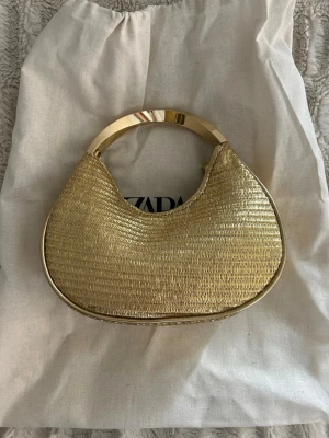 Guldig halvmåneformad handväska - Snygg guldig handväska från Zara i halvmåneform med metallhandtag.  Aldrig använd, dustbag medföljer