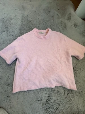 Ljusrosa stickad tröja Gina Tricot - Supersöt ljusrosa stickad tröja från Gina Tricot med korta ärmar och ribbade kanter. Tröjan har en rund halsringning och är gjord i ett mjukt material som känns skönt mot huden. Perfekt för dig som gillar en enkel men trendig look.