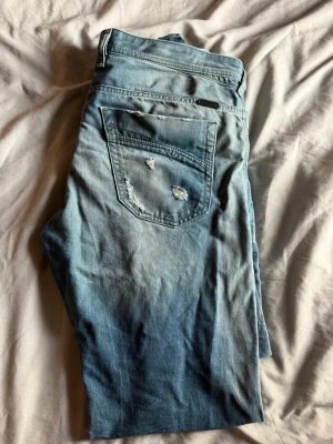 Diesel jeans - Säljer ett par ljusblå jeans från Diesel med slitningar och distressed detaljer på fickorna. Klassisk femficksmodell med snygg tvätt och Diesel Industry-märke på myntfickan. Perfekta för en avslappnad och trendig look.