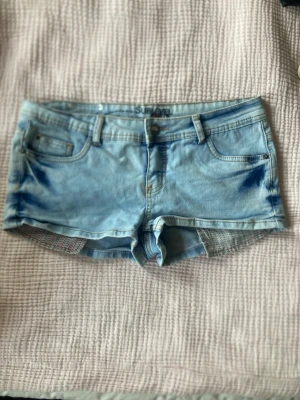 Ljusblå jeansshorts från Sublevel - Säljer ett par ljusblå jeansshorts från Sublevel med klassisk femficksdesign och bälteshällor. Shortsen har en snygg tvätt med blå detaljer vid fickorna och knappgylf. Perfekta för varma dagar och enkel att matcha med olika toppar.