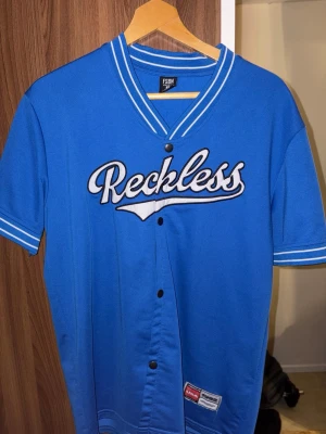 Blå baseball-inspirerad t-shirt Reckless - Snygg blå t-shirt med vit text 'Reckless'