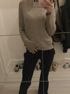 Beige stickad tröja med rund hals - En enkel och stilren beige stickad tröja med rund halsringning och långa ärmar. Tröjan har ribbstickade muddar vid ärmslut och nederkant. Perfekt att matcha med jeans eller kjol för en avslappnad look.