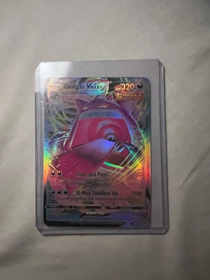 Pokémonkort Gengar VMAX Full Art - Säljer ett Pokémonkort med Gengar VMAX Full Art, holografiskt med färgglada regnbågseffekter. Kortet är från Sword & Shield-serien och har 320 HP. Levereras i plastficka för extra skydd. Perfekt för samlare eller Pokémonfans!