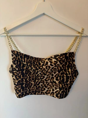 Leopardmönstrad croppad linnetopp - Snygg croppad linnetopp med leopardmönster och guldfärgade kedjeband. Materialet känns mjukt och följsamt mot huden.