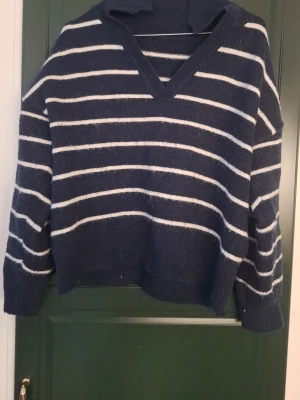 Mörkblå stickad tröja med ränder - Mysig mörkblå stickad tröja med via ränder. Den har en krage och V-ringad urringning. Nopprig och i använt skick.