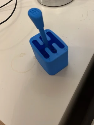 Blå växelspak i plast - Rolig blå växelspak i plast, formad som en klassisk manuell växelspak med siffror och spår för växlar. Perfekt som prydnad eller stressleksak på skrivbordet. Kompakt och lätt att ha med sig.