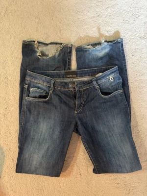 Blå jeans från Calvin Klein - Säljer ett par blå jeans med  slitna detaljer. Jeansen har klassisk femficksmodell, kontrastsömmar och dekorativa sömmar på bakfickorna. Perfekt för dig som gillar en unik och edgy stil.