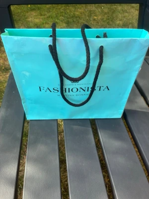 Fashionista bag med mode bok. - Äldre modebok som stått på en hylla som prydnad. Påsen har ”Tiffany” färg och boken som synes en annan nyans än påsen. Boken är oläst, bläddrat igenom någon gång. 