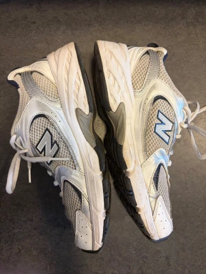 Vita New Balance sneakers mesh - Snygga vita sneakers från New Balance med meshpaneler och detaljer i silver och mörkblått. Skorna har en sportig design med klassisk N-logga på sidan och tjock sula för extra komfort. Perfekta för dig som gillar retrostil och streetwear.