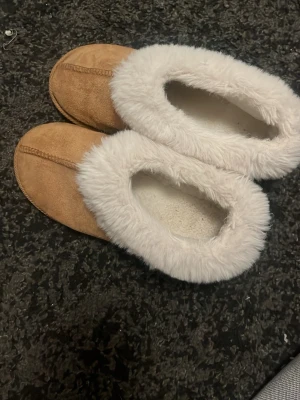 Söta tofflor - Säljer ett par mysiga bruna tofflor med vit fuskpäls, supersköna och passar perfekt nu när kallare tider närmar sig! Använda endast typ 3 ggr!! Är lite stor i storlek, jag som har 38 1/2 tycker att de är sköna att ha på aig men tar lite i tån längt fram! ( rekommenderar om du är 37/38) Skriv om ni har frågor eller prisförslag!!💗💗💗