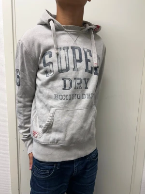 Superdry hoodie - Grå hoodie från Superdry i storlek S. Mycket bra skick. Modellen är 173cm, 64kg. Pris kan diskuteras!!