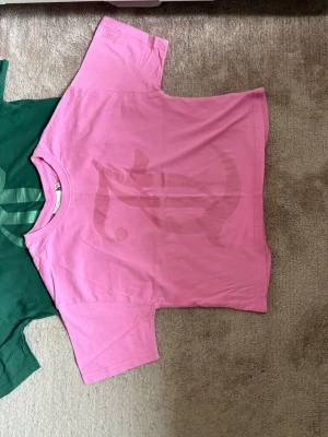 Rosa Juicy Couture t-shirt - Säljer en rosa t-shirt från Juicy Couture med ett stort, ton-i-ton tryck på framsidan. T-shirten har rund halsringning och korta ärmar. Perfekt för dig som gillar en avslappnad och trendig stil.