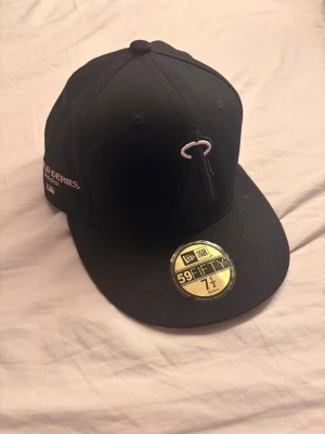 Svart New Era 59FIFTY keps - Snygg svart keps från New Era 59FIFTY med broderad logga framtill och rosa underskärm. På sidan finns World Series-brodyr och MLB-märke. Klassisk flat peak och strukturerad passform, perfekt för dig som gillar streetwear.