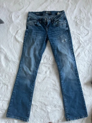 Blå bootcut jeans från LTB - Snygga blå bootcut jeans från LTB, modell VALERIE. Slitningar och tvättade detaljer för en avslappnad look. Tillverkade i mjukt denimtyg med dragkedjegylf och knapp. W28l32