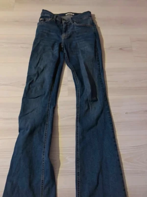 Blå bootcut jeans - Säljer ett par klassiska blå bootcut jeans med femficksmodell. Jeansen har en snygg tvätt och är tillverkade i ett mjukt denimtyg. Passar perfekt till sneakers eller boots och ger en retrovibe till din outfit.