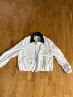 Vit jacka med kontrastkrage från Zara - Stilren vit jacka från Zara med svart krage i skinnimitation. Jackan har två stora fickor framtill, dragkedja och lång ärm. Perfekt för dig som gillar minimalistisk design med en twist.