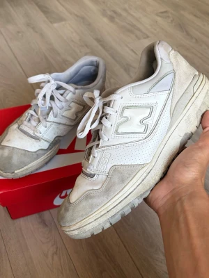 Vita New Balance 550 sneakers - Säljer ett par klassiska vita New Balance 550 sneakers med grå detaljer. Skorna har en chunky sula, perforerade paneler och snörning framtill. Tillverkade i en mix av läder och mocka för en stilren och sportig look.