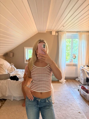 Randig ribbad linnetopp från H&M - Säljer en ribbad linnetopp från H&M i vitt med röda ränder. Toppen är croppad och ärmlös med rund halsringning. Perfekt för varma dagar och enkel att styla med jeans eller kjol.