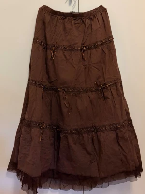 Söt, brun långkjol m/ spets & rosetter XL - Söt kjol köpt på myrorna för länge sedan! Ingen märke står. Storlek XL. Inga större fläckar eller andra defekter.