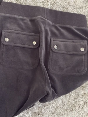 Mörkgrå mjukisbyxor med fickor - Säljer ett par mörkgrå mjukisbyxor i mjukt velourmaterial. Byxorna har raka ben och två stora bakfickor med lock och silvriga knappar. 