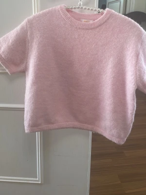 Ljusrosa fluffig kortärmad tröja - Supersöt ljusrosa tröja med korta ärmar och rund hals. Tröjan är fluffig och mjuk, perfekt för dig som gillar en cozy och trendig look. Passar till både jeans och kjol för en avslappnad stil. Lite smutsig på ryggen men man ser det inte jätte bra.