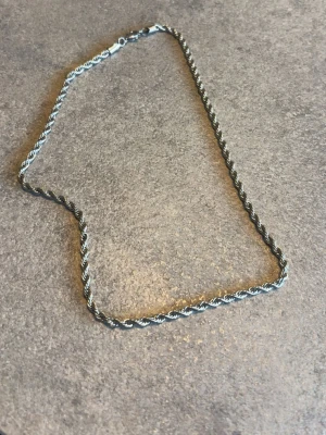 Silverfärgat tvinnat halsband - Säljer ett stilrent halsband i silverfärg i rostfritt stål. Halsbandet är ganska kort. 