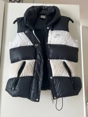 Svartvit väst från Nike - Jättefin retro väst från Nike.   Är tyvärr lite smutsig från användning. Därav är priset också nedsänkt på den. Vi har också skrivit ett namn i lapparna på den. Bilder finns på lapparna och vart den är smutsig. Den säljs i befintligt skick.   Storlek XS.