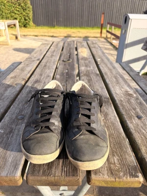 Svarta GGDB sneakers med stjärndetalj - Snygga svarta sneakers med GGDB/SSSTAR-tryck i guld på sidan och en stjärndetalj. Skorna har svart ovandel i läder, svart snörning och vit sula. Hälpartiet har en glittrig detalj som ger extra edge till looken. Perfekta för dig som gillar streetstyle.