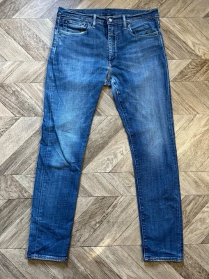 Levi's 512 - Snygga blå slim fit jeans med klassisk femficksdesign och lätt slitna detaljer. Jeansen har normal midja, dragkedjegylf och raka ben. Perfekta till en avslappnad stil och passar till det mesta. Materialet är denim i bomull med lite stretch för extra komfort. Längd 110cm Bredd 44cm