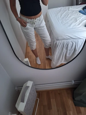 Vita vintage low waist capris byxor med knytband - Säljer ett par vita capris byxor med snörning i midjan och resår. Shortsen har bakfickor med knapp och avslappnad passform. Perfekta för sommaren och riktigt sköna att bära. Materialet känns lätt och luftigt. Passar storlek S-M