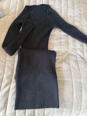 Svart ribbad långklänning - Säljer en svart ribbad långklänning med lång ärm och v-ringad hals. Klänningen har en tight passform och är tillverkad i ett stretchigt material som ger en snygg siluett. Perfekt för dig som gillar stilrena och enkla plagg.