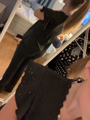 Svart blus med spets och volang - Svart blus med v-ringning, spetskant och volangdetaljer på de korta ärmarna. Tyget har små broderade hålmönster som ger en söt look men vid bröstet är det dubbeltyg så det ej syns igenom. fått av en kompis så vet ej vart den är från då den inte har någon lapp. vid frågor är det bara att skriva