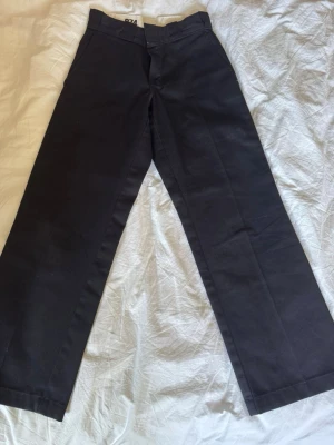 Svarta chinos från Dickies - Klassiska svarta chinos från Dickies med raka ben och normal midja. Byxorna har bälteshällor, två sidofickor fram och två bakfickor. Materialet är slitstarkt och har en lätt glansig finish. Perfekta för en clean och enkel stil.