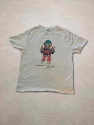 Vit t-shirt Polo Ralph Lauren björn - Vit t-shirt från Polo Ralph Lauren med björntryck på bröstet. Klassisk rund hals och korta ärmar. Tillverkad i mjuk bomull.
