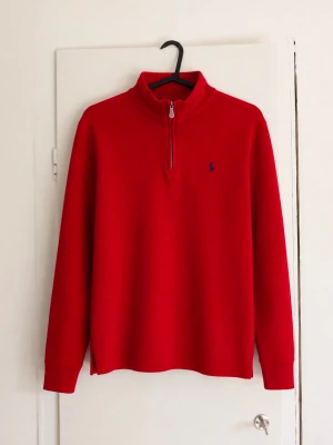 Ralph Lauren 1/4 zip - Säljer en klassisk röd halvzip från Ralph Lauren med broderad logga på bröstet. Perfekt för höst och vinter och enkel att styla både casual och lite mer uppklätt. • Färg: Röd med mörkblå logga • Modell: Half-zip / quarter zip • Skick:  Bra skick men har några skador! • Mjuk och bekväm passform • Passar både till jeans och chinos