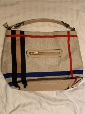 Beige handväska med färgglada ränder - Stilren handväska i beige tyg med röda, blå, svarta och bruna ränder. 