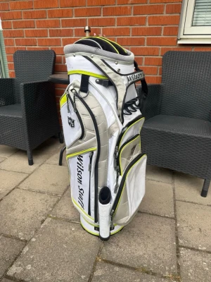 Wilson Staff vit vagnbag - Säljer en vit och grå golfbag från Wilson Staff med detaljer i limegrönt och svart. Väskan har flera praktiska fack, bärhandtag och plats för klubbor. Perfekt för dig som vill ha en snygg och funktionell golfbag till banan.