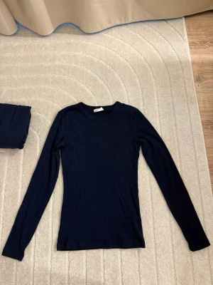Mörkblå långärmad tröja - En enkel och stilren mörkblå långärmad tröja med rund hals. Tröjan har en slim fit passform och är tillverkad i ett mjukt, stretchigt material som sitter skönt på kroppen. Perfekt att matcha med jeans eller kjol.