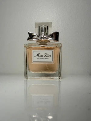 Miss Dior Eau de Toilette parfym - Miss Dior Eau de Toilette är en elegant parfym. Flaskan har en silverfärgad metallkork dekorerad med en söt rosett. Klassisk och feminin design som känns lyxig och tidlös.