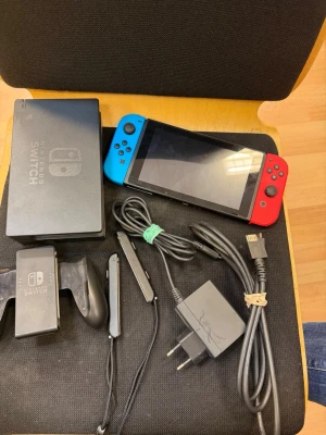Nintendo Switch med neonröda och blå Joy-Cons - Nintendo Switch spelkonsol med neonröda och blå Joy-Con-kontroller. Inkluderar dockningsstation, Joy-Con-grepp, handledsremmar, HDMI-kabel och laddare. Perfekt för gaming både hemma och på språng. Konsolen har en modern design i plast och glas.