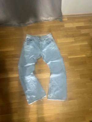 Jack&jones  - Säljer ett par jack&jones ljusblå jeans med rak passform och rå, fransig kant nedtill. Jeansen har klassisk femficksdesign och är tillverkade i denim. Perfekta för en avslappnad och trendig look.