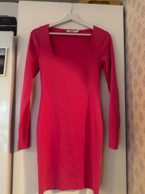Rosa långärmad klänning från NA-KD - Trendig rosa klänning från NA-KD med lång ärm och fyrkantig urringning. Klänningen är figurnära och har en enkel, stilren design som passar perfekt till olika tillfällen. Tillverkad i mjukt material för en bekväm känsla.