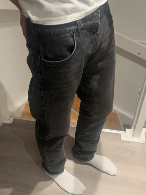 Mörkgrå raka jeans med tvättad look Woodbird - Säljer ett par mörkgrå jeans med tvättad finish och raka ben. Jeansen har klassisk femficksmodell och normal midja. Materialet är denim i bomull och passformen är avslappnad men ändå snyggt åtsittande. Perfekta för en chill och stilren outfit.