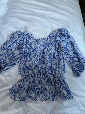Blåmönstrad blus från Kappahl - Säljer en luftig blus från Kappahl i storlek XS. Blusen har ett blått zebramönster, markerad midja och volang nedtill. Materialet är tunt och luftigt.  Ärmarna har en lätt puffig form och i ryggen så är det en rosett. Använd max 3 gånger. Pris kan diskuteras.
