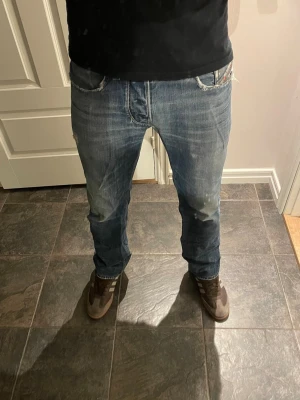 Diesel Larkee jeans med slitningar  - Säljer ett par blå jeans med slitningar och tvättade detaljer. Jeansen har raka ben, klassisk femficksmodell och låg midja. Perfekta för en avslappnad och trendig look. Materialet är denim i bomull. SE MÅTT PÅ BILDERNA