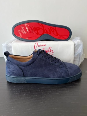 Blå mockasneakers från Christian Louboutin - Snygga sneakers i mörkblå mocka från Christian Louboutin med klassisk röd sula och diskret broderad logga på hälen. Skorna har snörning och en stilren design som passar perfekt till streetwear eller en mer dressad look. Allt OG medföljer förutom OG box
