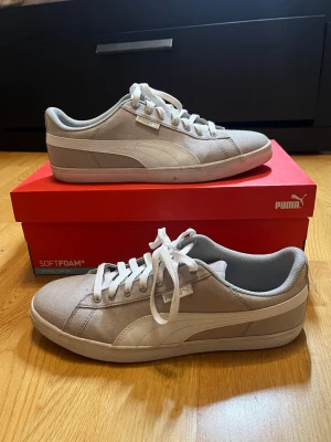Vita och gråa Puma sneakers - Säljer ett par Puma sneakers med snörning. Skorna är grå med vita detaljer och har en mjuk innersula för komfort. Yttersulan har ett mönster för bättre grepp. Skorna har tydliga tecken på användning men kan tvättas med rätt teknik. Skolåda som syns på bilden ingår. Vid frågor, extra bilder eller liknande är det bara att kontakta mig!
