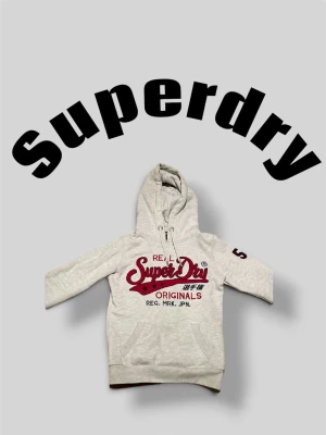 Superdry hoodie  - • ljusgrå Hoodie med röd text från superdry.          • Storlek XS.                                                                   •Nytt skick/mycket bra skick.                                    •skriv vid frågor, pris kan diskuteras👌🤝      