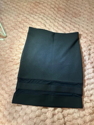 Svart pennkjol från Boohoo - Säljer en svart pennkjol från Boohoo med breda banddetaljer längst ner. Kjolen har en stilren och enkel design som passar till många olika looks. Materialet känns mjukt och stretchigt för en bekväm passform.